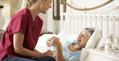 A female patient at home in bed being visited by a nurse